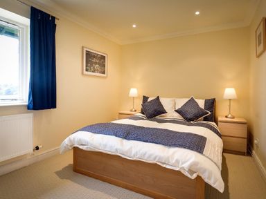 A bedroom with a double bed blue and white bedding lamps on bedside tables and a window with blue curtains at The Old Barn in Ambleside