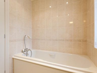 A bathroom with a bathtub and handheld shower on tiled walls at The Old Barn in Ambleside