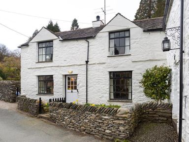 A white stone cottage with black window frames and a small stone wall garden at Camellia Cottage in Bowness