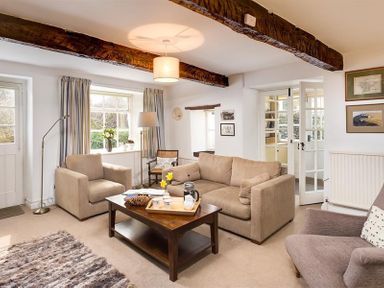 A living room with sofas armchairs a wooden coffee table and exposed wooden beams at Camellia Cottage in Bowness