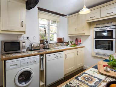A kitchen with cream cabinets appliances a washing machine and dishwasher at Camellia Cottage in Bowness