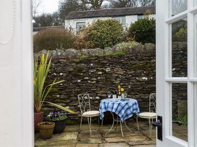 A small outdoor patio area with a table covered by a blue checkered tablecloth and two metal chairs with cushions at Camellia Cottage in Bowness