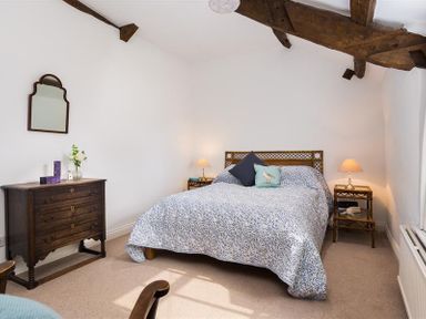 A bedroom with a bed side tables a dresser with a mirror and exposed wooden ceiling beams at Camellia Cottage in Bowness