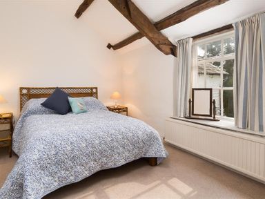 A bedroom with a bed two bedside tables with lamps exposed wooden ceiling beams and a window with curtains at Camellia Cottage in Bowness
