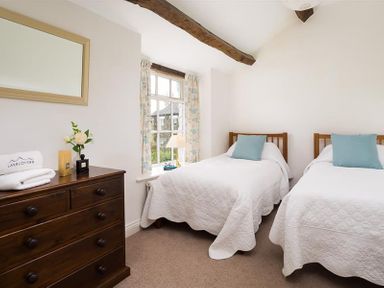 A bedroom with two single beds wooden dresser and window with curtains at Camellia Cottage in Bowness