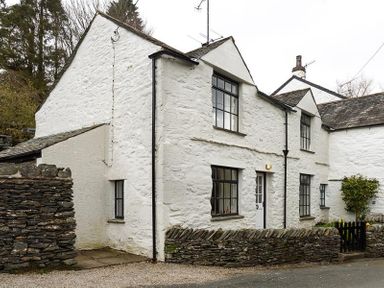 A white stone house with black framed windows and a stone wall at Camellia Cottage in Bowness