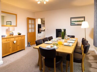 A dining room with a wooden table set for eight people and a wooden sideboard with a lamp and fruit bowl at Bowderstone in Keswick