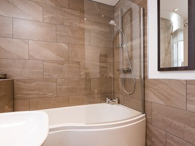 A bathroom with a bathtub shower combination and a mirror on the wall at Bowderstone in Keswick
