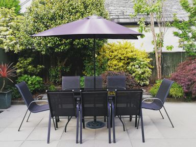 An outdoor patio with a table and eight chairs under a large umbrella surrounded by plants and trees at Bowderstone in Keswick