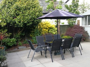An outdoor patio with a dining table and eight chairs under a large umbrella surrounded by plants at Bowderstone in Keswick