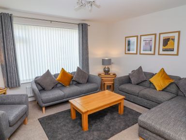 A living room with gray sofas and chairs yellow cushions a wooden coffee table and framed pictures on the wall at Bowderstone in Keswick