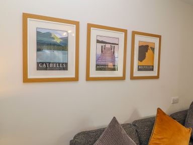 Three framed posters of Catbells Derwentwater and Helvellyn above a grey sofa with cushions at Bowderstone in Keswick
