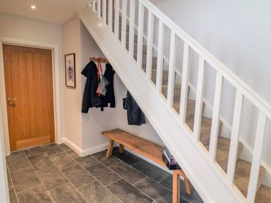 An entryway with a wooden door coat hooks with jackets a wooden bench and stairs with beige carpet at Bowderstone in Keswick