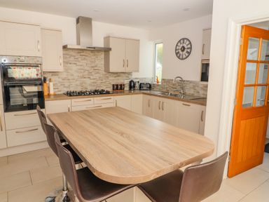A kitchen with a wooden island countertop and bar stools next to cabinets with built in oven and stove at Bowderstone in Keswick