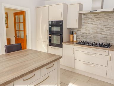 A kitchen with a wooden countertop island a gas stove double oven and tiled backsplash at Bowderstone in Keswick