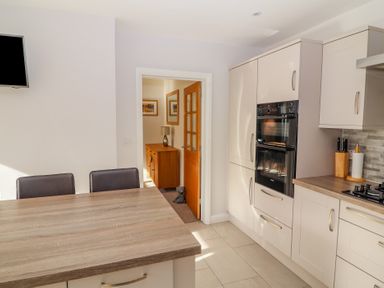 A kitchen with white cabinets a built in oven a cooktop and a wooden table with chairs at Bowderstone in Keswick