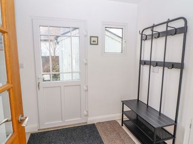 An entryway with a white door, small window, black metal coat rack with bench, and two floor mats at Bowderstone in Keswick
