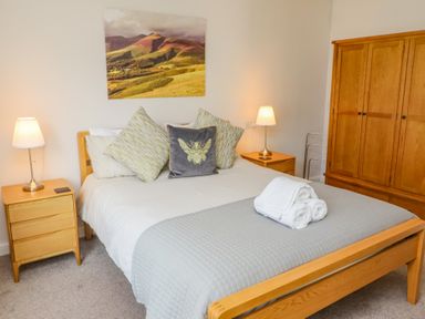 A bedroom with a wooden bed frame, bedside tables with lamps, a wooden wardrobe, and a landscape picture above the bed at Bowderstone in Keswick