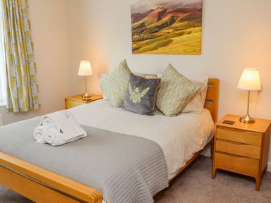 A bedroom with a wooden bed and bedside tables with lamps at Bowderstone in Keswick