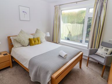 A bedroom with a wooden bed a gray quilt and pillows a wooden bedside table a gray armchair with a pillow and a large window at Bowderstone in Keswick