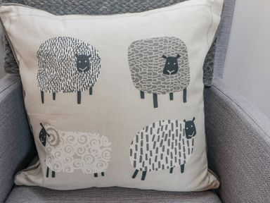 A cushion with illustrations of four sheep on a grey fabric chair at Bowderstone in Keswick
