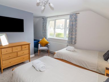 A bedroom with two single beds a wooden dresser a chair with a cushion and a window with curtains at Bowderstone in Keswick