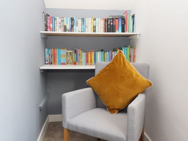 A small reading nook with a gray armchair and a mustard pillow in front of two shelves filled with books at Bowderstone in Keswick