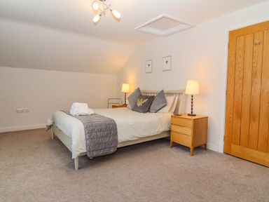 A bedroom with a bed between two wooden bedside tables with lamps and a wooden door at Bowderstone in Keswick