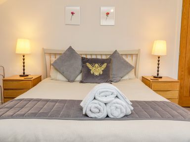 A bedroom with a bed with three pillows and three rolled towels on a grey runner at Bowderstone in Keswick