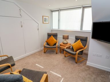 A sitting room with three chairs two throw pillows a side table with a lamp a wall-mounted tv and storage cupboards at Bowderstone in Keswick