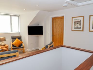 A living room area with armchairs a wall-mounted TV wooden door and framed pictures at Bowderstone in Keswick