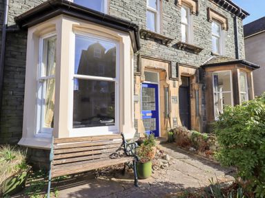 A stone house exterior with bay windows a blue door and a wooden bench with plants outside at Number Twenty in Keswick