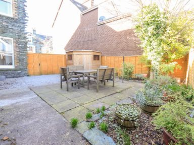 A backyard with a wooden table and four chairs on a stone patio and garden pots at Number Twenty in Keswick