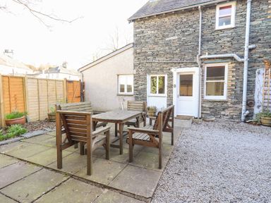 A backyard with wooden outdoor table and chairs a stone house exterior and a gravel area at Number Twenty in Keswick