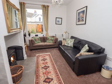 A living room with two sofas a fireplace a window with curtains and framed pictures on the walls at Number Twenty in Keswick