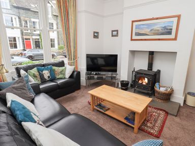 A living room with black leather sofas and a wooden coffee table near a wood burning stove and a TV at Number Twenty in Keswick