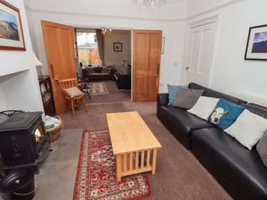 A sitting room with a black sofa with cushions a wooden coffee table a wood burning stove and open double wooden doors leading to another room at Number Twenty in Keswick