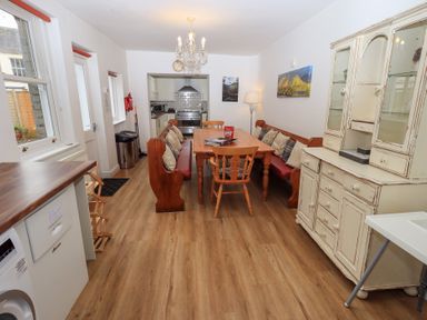 A dining area with wooden table benches chairs a white cabinet and kitchen appliances at Number Twenty in Keswick