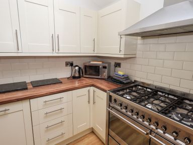 A kitchen with white cabinets wooden countertops a metal stove a microwave a kettle and folded towels at Number Twenty in Keswick