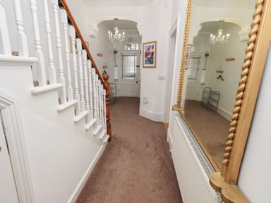 A hallway with carpeted floor a staircase on the left a large framed mirror on the right and a chandelier hanging from the ceiling at Number Twenty in Keswick