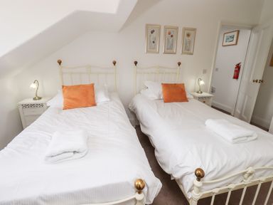 A bedroom with two single beds with white bedding and orange pillows at Number Twenty in Keswick