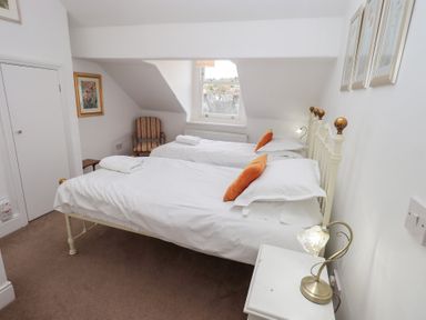 A bedroom with two single beds with white bedding and orange pillows a chair a bedside table with a lamp and a window at Number Twenty in Keswick