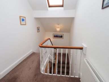 A stairwell with white walls brown carpet and wooden handrail at Number Twenty in Keswick