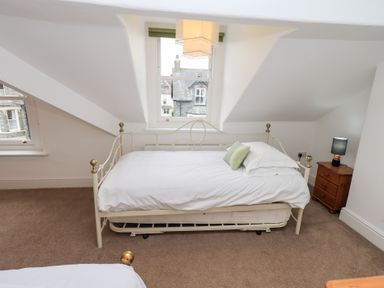 A bedroom with a white metal framed bed with white bedding and a green pillow next to a wooden nightstand with a lamp and windows at Number Twenty in Keswick