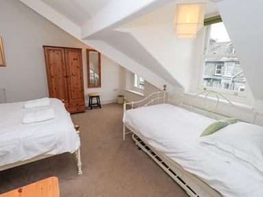 A bedroom with two single beds a wooden wardrobe mirror and windows under sloped ceilings at Number Twenty in Keswick