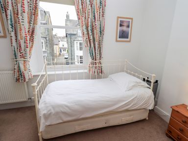 A bedroom with a white metal bed near a window with patterned curtains and a wooden bedside table at Number Twenty in Keswick