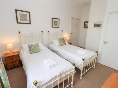 A bedroom with two single beds with white bedding and pillows a nightstand with a lamp between the beds and framed pictures on the walls at Number Twenty in Keswick