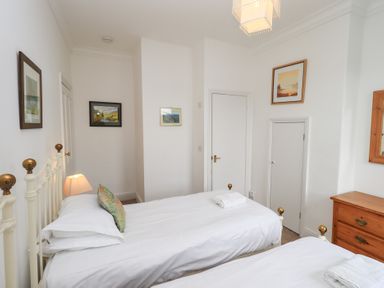 A bedroom with two single beds white walls framed pictures and a wooden dresser at Number Twenty in Keswick