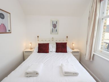 A bedroom with a double bed two red pillows two folded towels bedside tables with lamps and a window at Number Twenty in Keswick