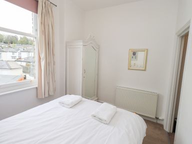 A bedroom with a bed, two folded towels, a window with curtains, a white wardrobe with a mirror, a radiator, and a wall mirror at Number Twenty in Keswick
